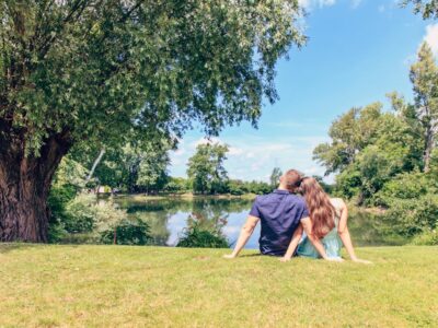 Couple Sitting on Grass Field in Front of Body of Water