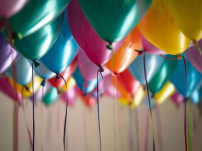 Rows of multicoloured helium balloons with ribbons hanging in a celebration venue
