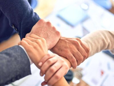 Close-up of four people gripping each other's wrists in a team huddle over an office desk