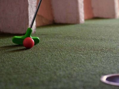 Green mini-golf putter and red ball on an adventure golf putting surface with the hole ahead
