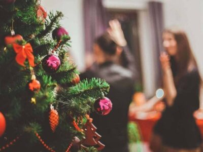 Close-up of a decorated Christmas tree with pink baubles and bows, party guests blurred behind