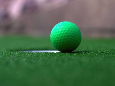 Bright green golf ball resting at the edge of a hole on an adventure golf putting green