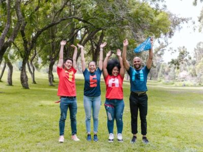 Four people in team T-shirts raising their arms in celebration on a green outdoor field