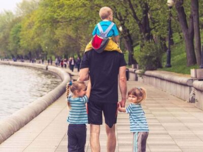 Adult walking along a riverside path with three young children on a sunny day out
